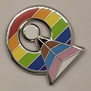 Könnte beinhalten: Eine silberne Anstecknadel mit einem Regenbogenkreis und einer weißen, schwarzen, braunen, blauen und pinkfarbenen geometrischen Form in der Mitte.
