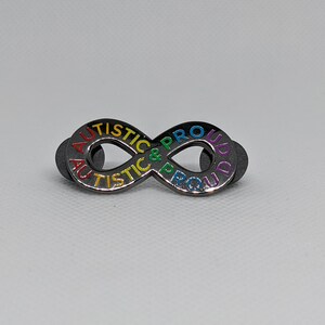 K&ouml;nnte beinhalten: Eine silberne Unendlichkeits-Symbol-Anstecknadel mit den Worten "Autistic & Proud" in Regenbogenfarben darum herum.