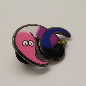 May include: A pink and purple worm with googly eyes is curled around a blue and black crescent moon with yellow stars. The worm and moon are attached to a metal pin back.