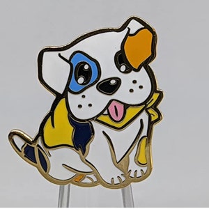 Puede incluir: Un pin de esmalte que representa a un perro de dibujos animados con detalles azules, naranjas y amarillos. El perro lleva un pañuelo amarillo con ribete azul marino.