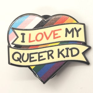 Pode incluir: Um broche em forma de coração com um design de bandeira arco-íris e uma faixa que diz "Eu amo meu filho queer".