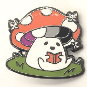 May include: A white mushroom with a red and white cap, holding a red book. The mushroom is sitting on a green patch of grass. The mushroom has a black and white face with a purple and white stripe on the cap.