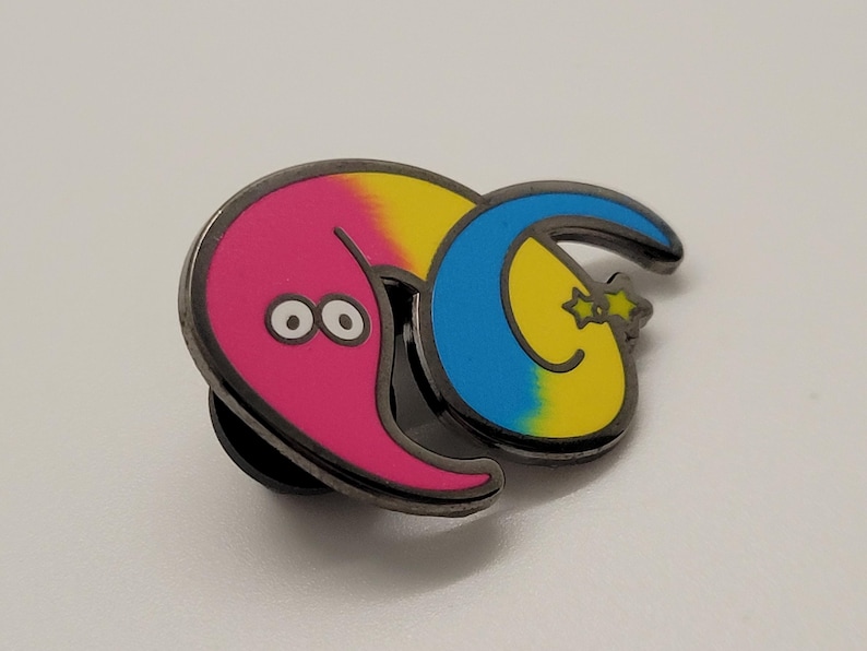 May include: A pink and yellow worm with blue and yellow stripes and two black eyes. The worm is curled up and has a black star on its tail. The worm is a metal pin.
