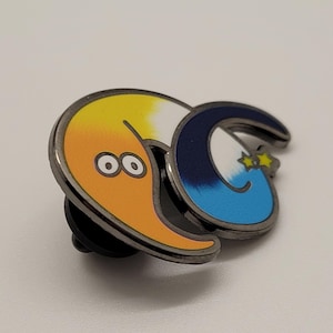 May include: A metal pin featuring a cartoon worm with a yellow and orange body, a blue and white tail, and two black eyes. The worm is curled into a circle with its tail in its mouth.