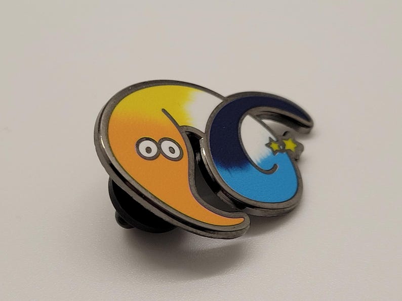 May include: A metal pin featuring a cartoon worm with a yellow and orange body, a blue and white tail, and two black eyes. The worm is curled into a circle with its tail in its mouth.
