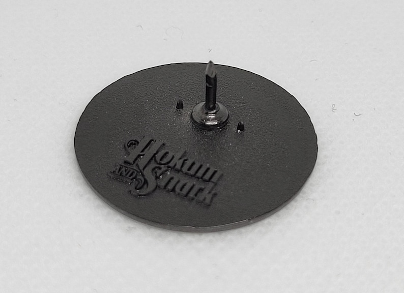 K&ouml;nnte beinhalten: Schwarzer Metallstift mit kreisf&ouml;rmigem Design. Der Stift tr&auml;gt den Text "Hokum & Smack" in einer stilisierten Schrift.