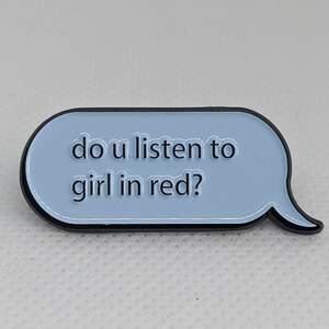 May include: A blue and black enamel pin shaped like a speech bubble with the text "do u listen to girl in red?"