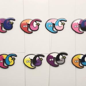 May include: Set of ten enamel pins featuring two worm-like figures intertwined. Each pin is a different color combination, including pink and purple, red and pink, blue and pink, pink and black, purple and gray, yellow and purple, pink and blue, orange and blue, and black and gray.