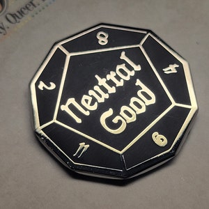 May include: A black and silver metal pin shaped like a D8 dice with the words "Neutral Good" in gold lettering.