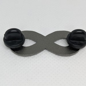 K&ouml;nnte beinhalten: Eine silberne Unendlichkeits-Anstecknadel mit schwarzen Gummibeschl&auml;gen. Die Anstecknadel ist ein beliebtes Symbol f&uuml;r ewige Liebe und Freundschaft.