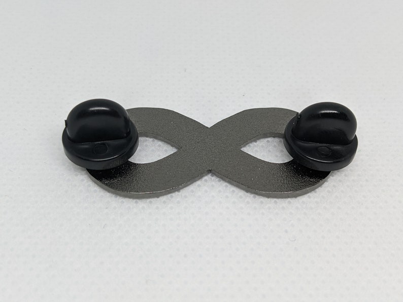 K&ouml;nnte beinhalten: Eine silberne Unendlichkeits-Anstecknadel mit schwarzen Gummibeschl&auml;gen. Die Anstecknadel ist ein beliebtes Symbol f&uuml;r ewige Liebe und Freundschaft.