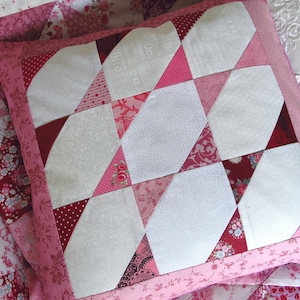 Può includere: Un cuscino patchwork rosa e bianco con un design geometrico. Il cuscino è realizzato con diversi tessuti con motivi diversi, tra cui pois, stampe floreali e paisley.