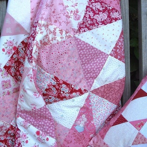 May include: A pink and white patchwork quilt with a floral pattern. The quilt is made of various fabrics with different floral designs and is arranged in a geometric pattern.