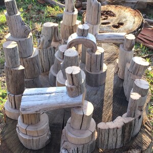 May include: A collection of natural wood blocks stacked to create a whimsical structure. The blocks are various sizes and shapes, with a natural, weathered finish. The blocks are arranged on a tree stump.