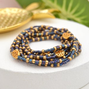 Könnte beinhalten: Ein mehrreihiges Perlenarmband mit goldenen Akzenten. Das Armband besteht aus dunkelblauen und goldenen Perlen und weist ein sich wiederholendes Muster aus kleinen goldenen Perlen und größeren goldenen Perlen mit einem dekorativen Design auf.