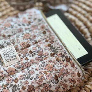 May include: A floral print e-reader case with a gold zipper, holding an e-reader. The case features a cream background with a pattern of small pink and brown flowers and green leaves. The label reads "the mini peace".
