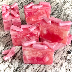 Pode incluir: V&aacute;rias barras de sab&atilde;o rosa e branco com redemoinhos, cada uma coberta com decora&ccedil;&otilde;es rosa em forma de cristal. O sab&atilde;o tem um efeito marmorizado. Os enfeites de cristal s&atilde;o de um tom rosa mais claro e s&atilde;o colocados em cima das barras de sab&atilde;o.