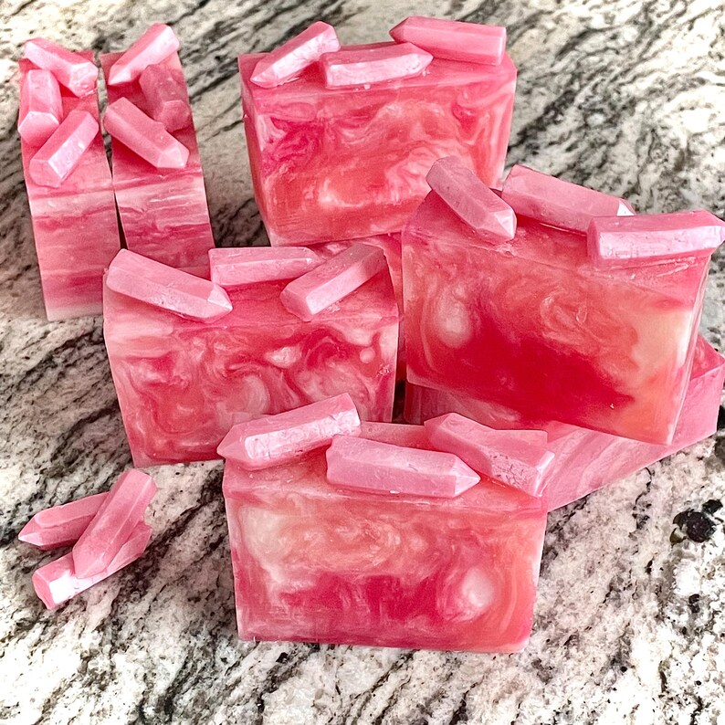 Pode incluir: V&aacute;rias barras de sab&atilde;o rosa e branco com redemoinhos, cada uma coberta com decora&ccedil;&otilde;es rosa em forma de cristal. O sab&atilde;o tem um efeito marmorizado. Os enfeites de cristal s&atilde;o de um tom rosa mais claro e s&atilde;o colocados em cima das barras de sab&atilde;o.