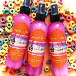 May include: Three pink 4 oz bottles of Fruitopia Sweet Shop Twinkles fragrance spray. The bottles are labeled with the product name and website address. The bottles are surrounded by colorful cereal rings.