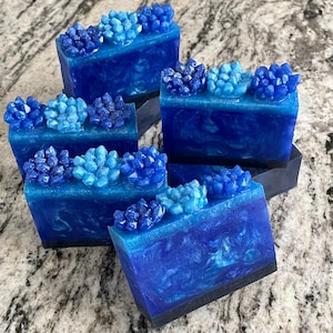 May include: Several bars of handmade soap in shades of blue, with a crystal-like design on top. The soap has a marbled appearance with varying shades of blue and white. The crystal design is a gradient of blue hues.
