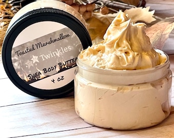 May include: A 4 ounce jar of Toasted Marshmallow Twinkles Shea Body Butter. The jar is clear and shows the creamy, light brown body butter inside. The label on the jar is black with white text and a star design.