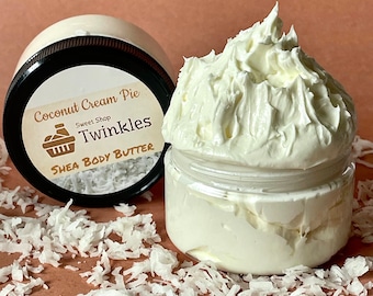 May include: A white shea body butter in a clear jar with a white label that reads "Coconut Cream Pie Sweet Shop Twinkles Shea Body Butter". The jar is sitting on a brown surface with shredded coconut.