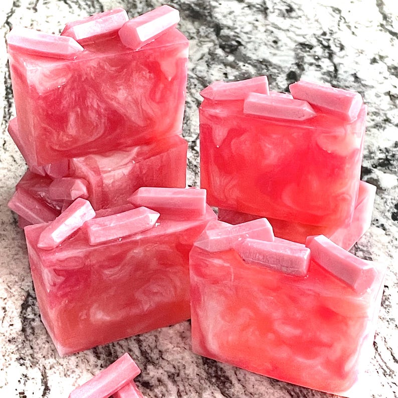 Pode incluir: Barras de sab&atilde;o rosa e branco com redemoinhos e detalhes em forma de cristal. As barras de sab&atilde;o s&atilde;o empilhadas e dispostas sobre uma superf&iacute;cie salpicada. O sab&atilde;o tem uma apar&ecirc;ncia transl&uacute;cida com efeito marmorizado.