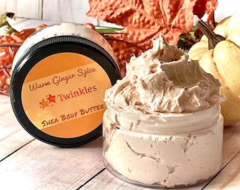May include: A clear jar filled with a light brown shea body butter. The jar has a black lid with a label that reads "Warm Ginger Spice Twinkles Shea Body Butter".