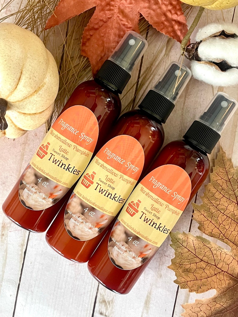 May include: Three 4 ounce bottles of brown liquid fragrance spray with white labels. The labels feature a brown and white illustration of a cup of coffee with whipped cream and a shopping cart icon. The text on the labels reads "Fragrance Spray", "Marshmallow Pumpkin Latte", "Sweet Shop", and "Twinkles". The bottles are on a light brown wooden surface.