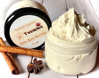 May include: A 4 ounce jar of Spiked Eggnog Shea Body Butter by Twinkles. The jar is filled with a creamy, white body butter. The jar is sitting on a white wooden surface with cinnamon sticks and a star anise.