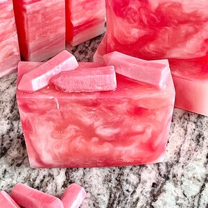 Pode incluir: Barras de sab&atilde;o rosa e branco com redemoinhos e pe&ccedil;as retangulares. O sab&atilde;o tem uma apar&ecirc;ncia marmorizada, com diferentes tons de rosa e branco. V&aacute;rias barras s&atilde;o vis&iacute;veis, algumas com pe&ccedil;as de destaque.