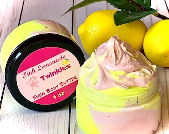 May include: A jar of Pink Lemonade Twinkles Shea Body Butter, with a pink and yellow swirl design, sits next to two lemons. The label reads "Pink Lemonade Twinkles Shea Body Butter 4 oz."