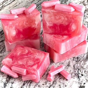 Pode incluir: V&aacute;rias barras de sab&atilde;o rosa artesanais com um design em espiral e pequenos detalhes em forma de cristal. As barras de sab&atilde;o s&atilde;o empilhadas e dispostas sobre uma superf&iacute;cie clara, mostrando sua cor vibrante e textura &uacute;nica.