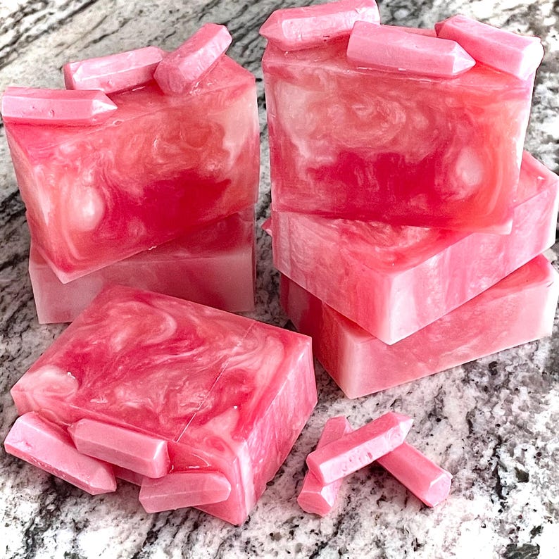 Pode incluir: V&aacute;rias barras de sab&atilde;o rosa artesanais com um design em espiral e pequenos detalhes em forma de cristal. As barras de sab&atilde;o s&atilde;o empilhadas e dispostas sobre uma superf&iacute;cie clara, mostrando sua cor vibrante e textura &uacute;nica.