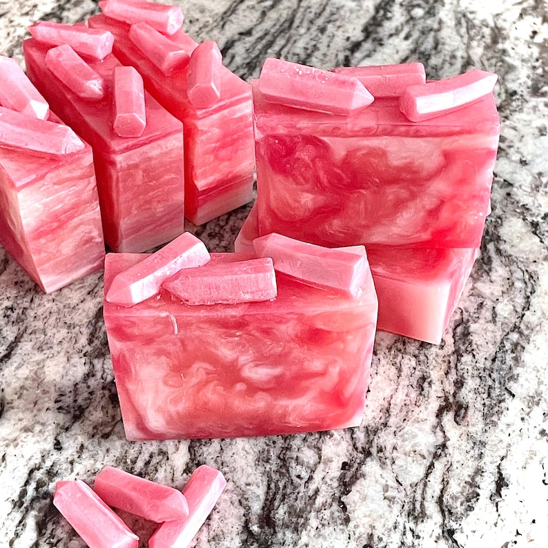 Pode incluir: Barras de sab&atilde;o rosa e branco com redemoinhos e detalhes em forma de cristal rosa. As barras de sab&atilde;o t&ecirc;m formato retangular e s&atilde;o dispostas sobre uma superf&iacute;cie salpicada. Os detalhes de cristal s&atilde;o colocados em cima.