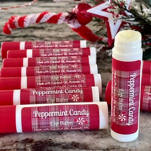 May include: A collection of red and white lip balm tubes with "Peppermint Candy" labels. The labels feature a plaid design and a peppermint candy graphic. The lip balms are made with coconut oil and avocado oil.