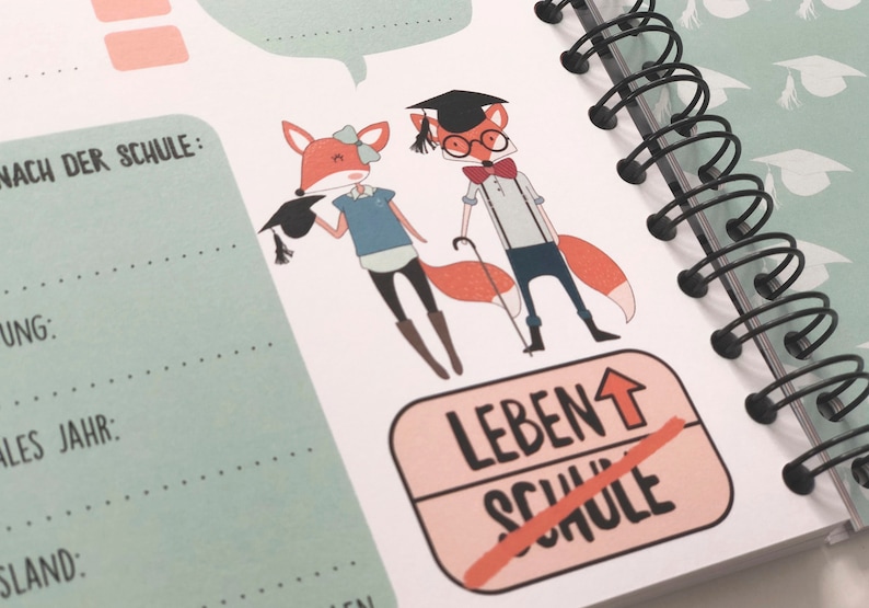Op de afbeelding: Een roze en witte sticker met de tekst "LEBEN&uarr; SCHULE" met een rode streep door "SCHULE". Op de achtergrond zijn twee cartoonvossen te zien die een afstudeerpet dragen. De vossen zijn oranje met witte accenten en dragen verschillende outfits.