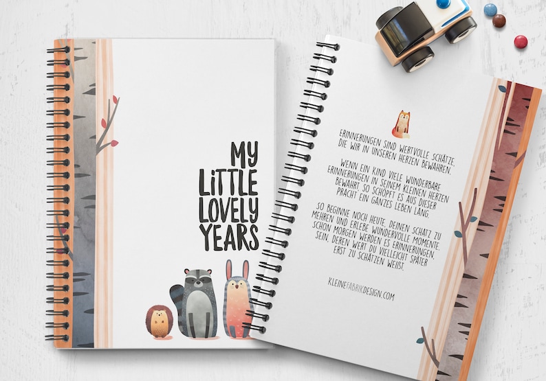 Puede incluir: Un cuaderno de espiral con una cubierta blanca y el texto "My Little Lovely Years" en negro. La cubierta presenta una ilustraci&oacute;n de acuarela de un mapache, un conejo y un erizo en un entorno de bosque. La contraportada tiene una cita en alem&aacute;n sobre el valor de atesorar los recuerdos.