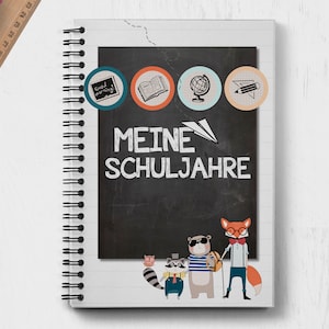 Op de afbeelding: Een wit spiraalnotitieblok met een zwarte schoolbordomslag. Het schoolbord heeft de tekst "MEINE SCHULJAHRE" erop geschreven. Bovenaan het schoolbord staan vier kleurrijke cirkels met pictogrammen die een boek, een wereldbol, een potlood en een klok voorstellen. Onderaan het schoolbord staan vijf cartoondieren.