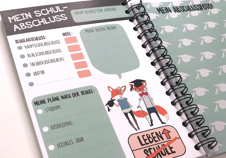 Op de afbeelding: Een groen en wit spiraalnotitieblok met een afstudeerthema. De omslag toont een vos die een afstudeerpet draagt en een diploma vasthoudt. De tekst op de omslag luidt "Mein Schul-Abschluss" en "Mein Abschlussfoto!"