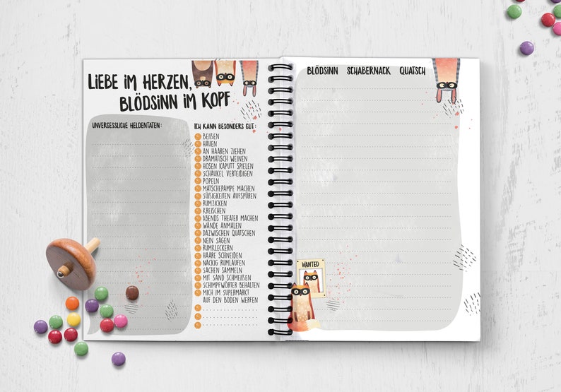 Puede incluir: Una libreta de espiral gris y blanca con una ilustraci&oacute;n de un gato en la portada. El texto de la portada dice "Liebe im Herzen, Bl&ouml;dsinn im Kopf". La libreta tiene una lista de "Unvergessliche Heldentaten" y "Ich kann besonders gut" con una lista de actividades.
