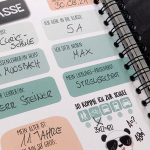 Op de afbeelding: Een schoolplanner met een zwart-witte pandabeerillustratie. De planner heeft een zwarte spiraalbinding en bevat een checklist voor het klaar maken voor school, inclusief lopen, fietsen, de bus nemen en de trein nemen. De planner bevat ook een sectie voor persoonlijke informatie, zoals de naam van de leerling, de leeftijd, de naam van de school, de naam van de leraar en de favoriete snack.