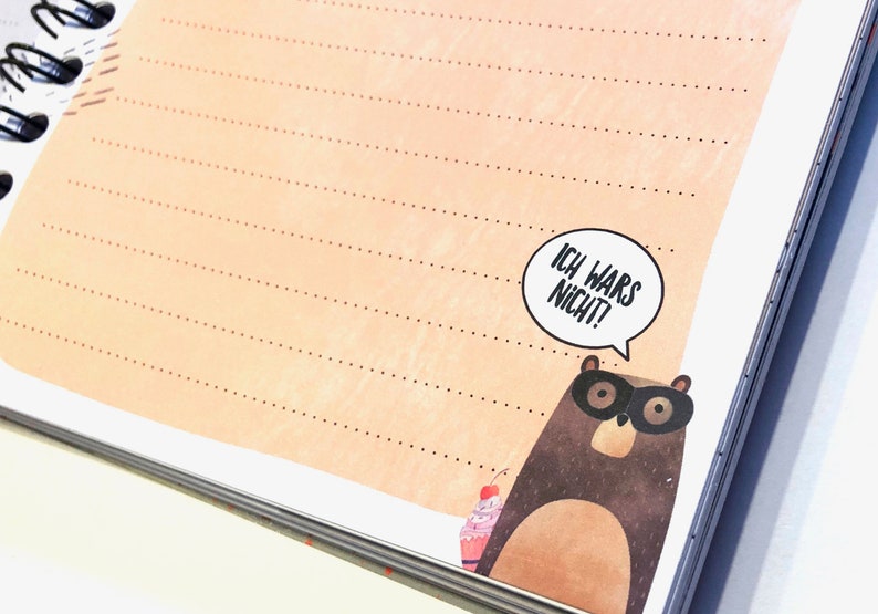 Puede incluir: Una libreta de notas marr&oacute;n claro con un patr&oacute;n de l&iacute;neas punteadas y un oso de dibujos animados con un globo de di&aacute;logo que dice "Ich wars nicht!" (&iexcl;No fui yo!).