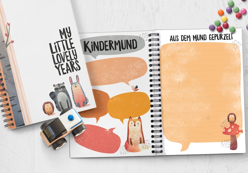 Puede incluir: Un cuaderno blanco de espiral con una ilustraci&oacute;n colorida de animales y burbujas de di&aacute;logo. La portada dice "My Little Lovely Years" y "Kindermund" con el texto "Aus dem Mund Gepurzel" en el lado derecho.