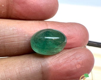 May include: A vibrant green oval-shaped emerald gemstone. The emerald has a smooth, polished surface and is held in a hand.