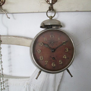May include: A silver alarm clock with a red face and black hands. The clock has a bell on top and three legs.