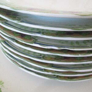 May include: A stack of vintage white porcelain plates with a green and brown floral design. The plates have a blue trim and are in good condition.