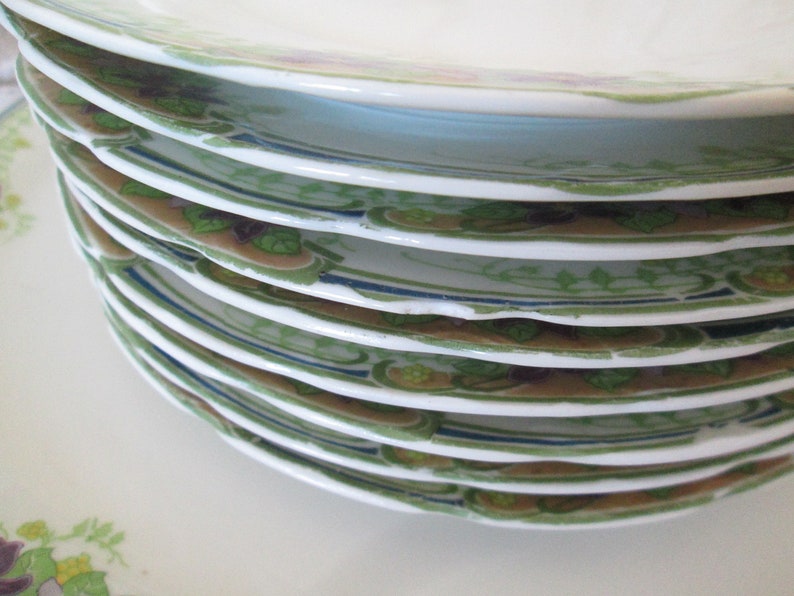 May include: A stack of vintage white porcelain plates with a green and brown floral design. The plates have a blue trim and are in good condition.