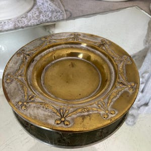 Könnte beinhalten: Eine runde, antike Messingplatte mit einem goldenen Zentrum und einem silberfarbenen Rand. Der Rand weist geprägte goldene Blumenmuster auf. Die Platte ist wahrscheinlich Vintage und weist Gebrauchsspuren auf.