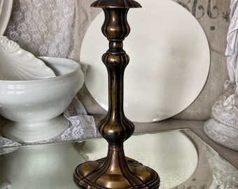 May include: A tall, antique brass candlestick with a fluted design. The candlestick has a round base and a single candle holder.